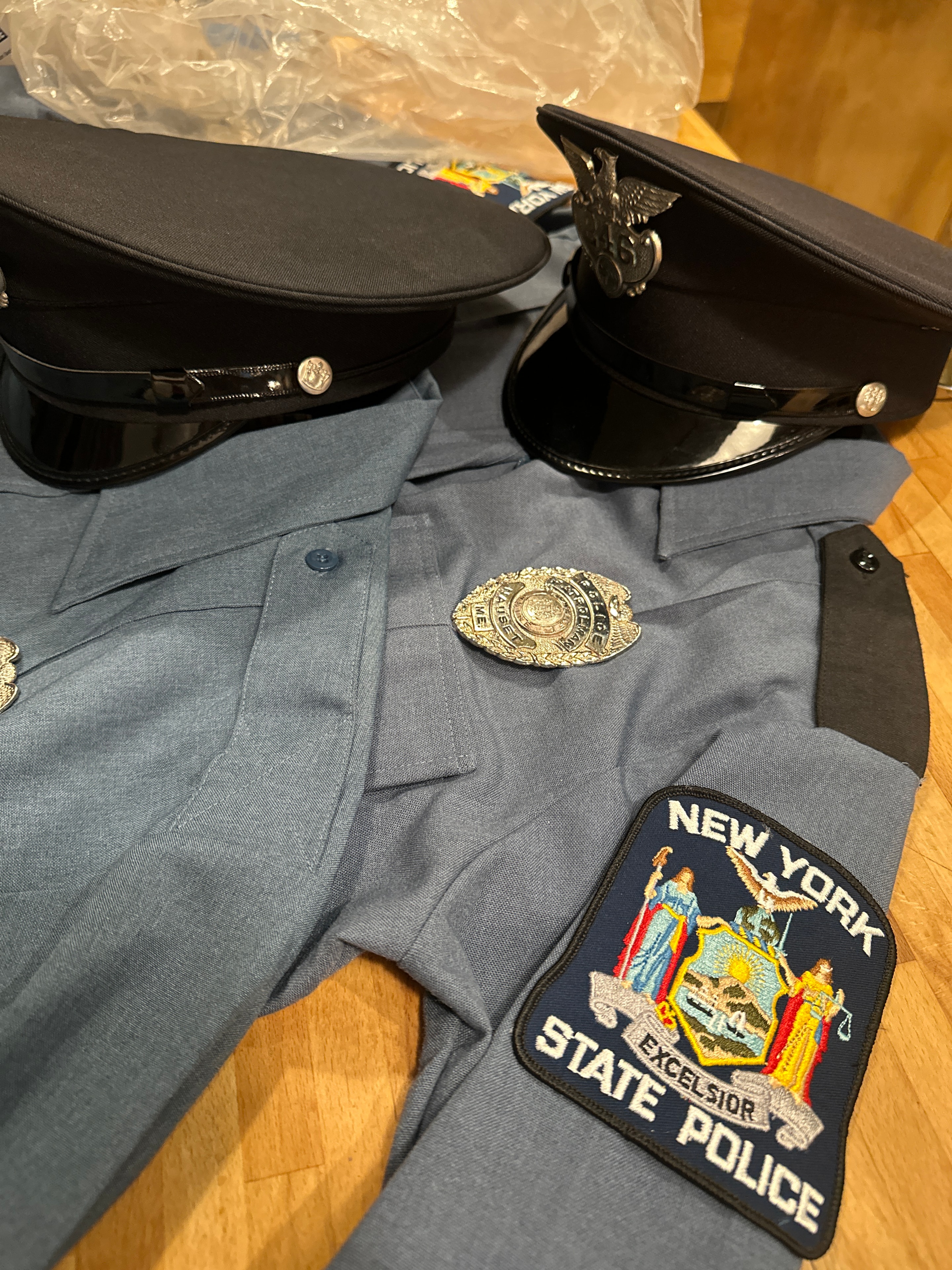 New York State Police uniform — grey-blue shirt with NY State Police shoulder patch, trooper cap, and police badge