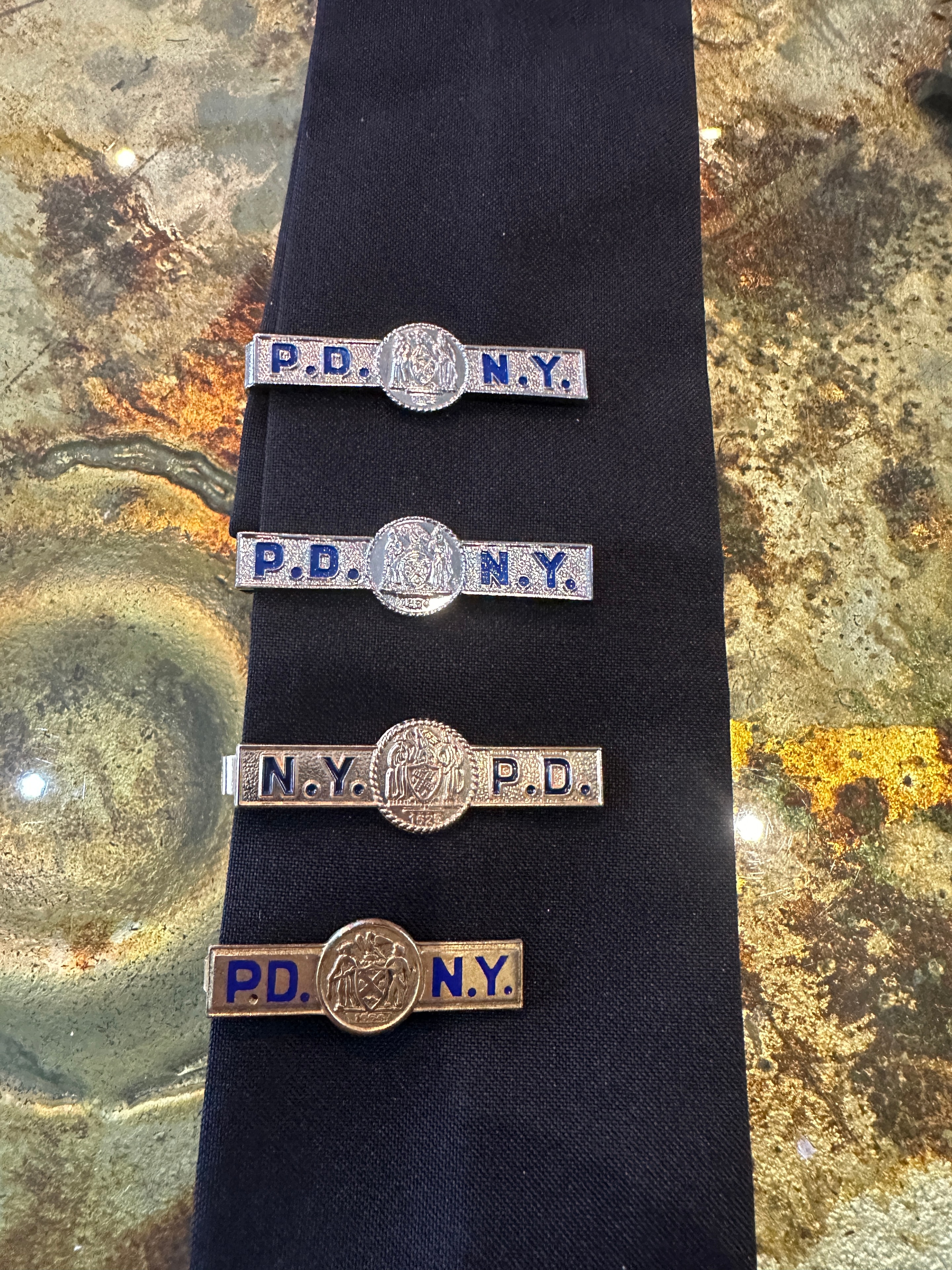 Vintage NYPD and P.D.N.Y. tie clips in silver and gold with blue enamel lettering displayed on navy police tie
