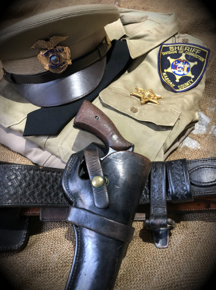 Vintage country police officer uniform — Nassau County Sheriff cap, tan shirt with badge, and black leather duty belt with holster