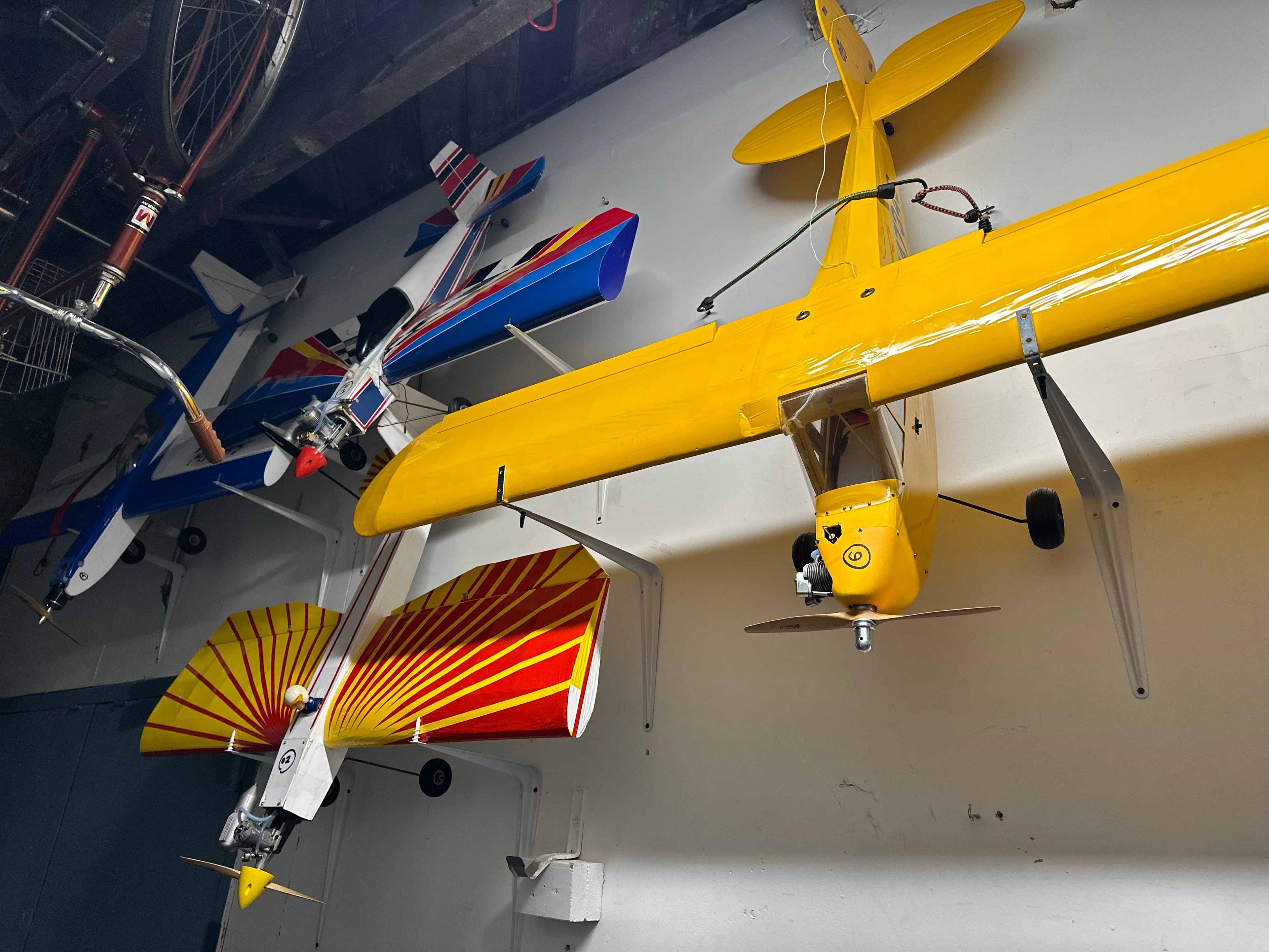 Collection of large-scale vintage R/C model planes mounted on wall including yellow monoplane, blue and red aerobatic planes, and red sunburst design